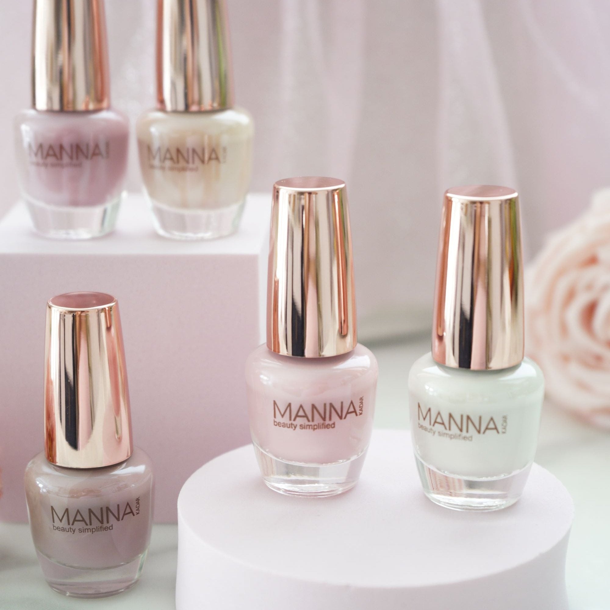5 Nail polish bottles with gold caps on small pedestals in neutral pastel shades of pink, cream, white, and tan by Manna Kadar.