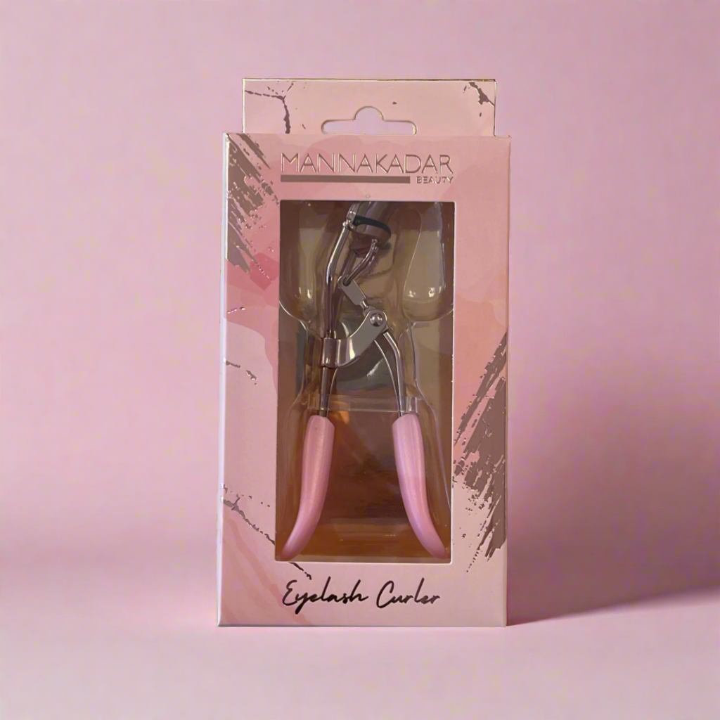 Manna Kadar pink handle eyelash curler in pink box with gold foil painterly swipes on it sitting on pink background