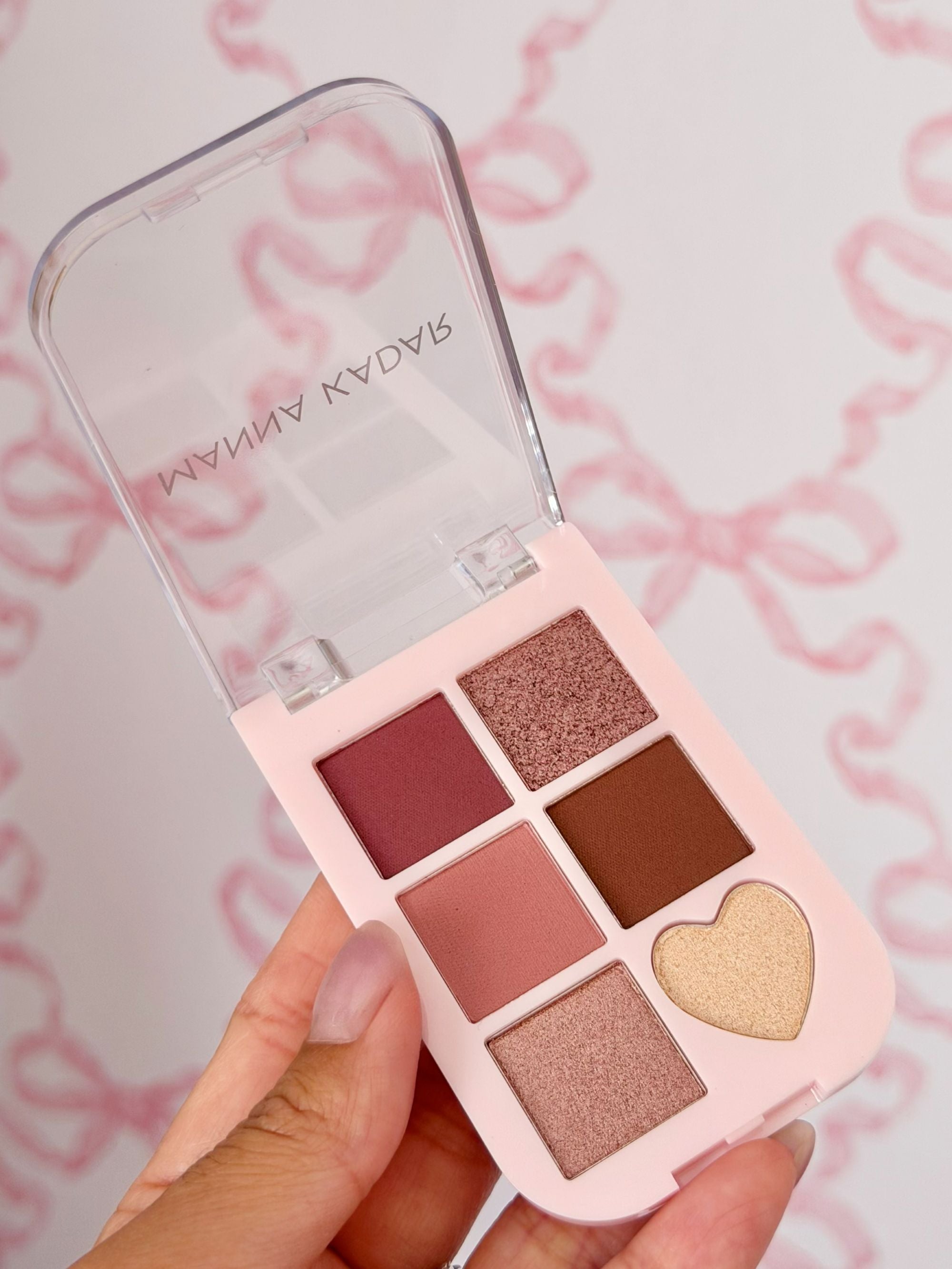 Makeup palette with heart-shaped design held by a hand against a pink background