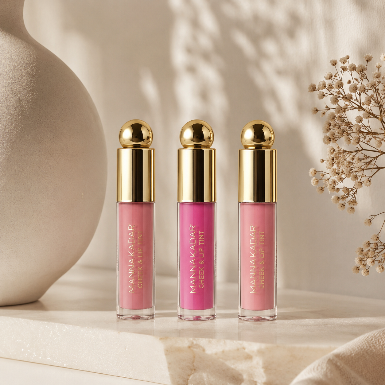 Three pink lip tint bottles with gold caps on a neutral background