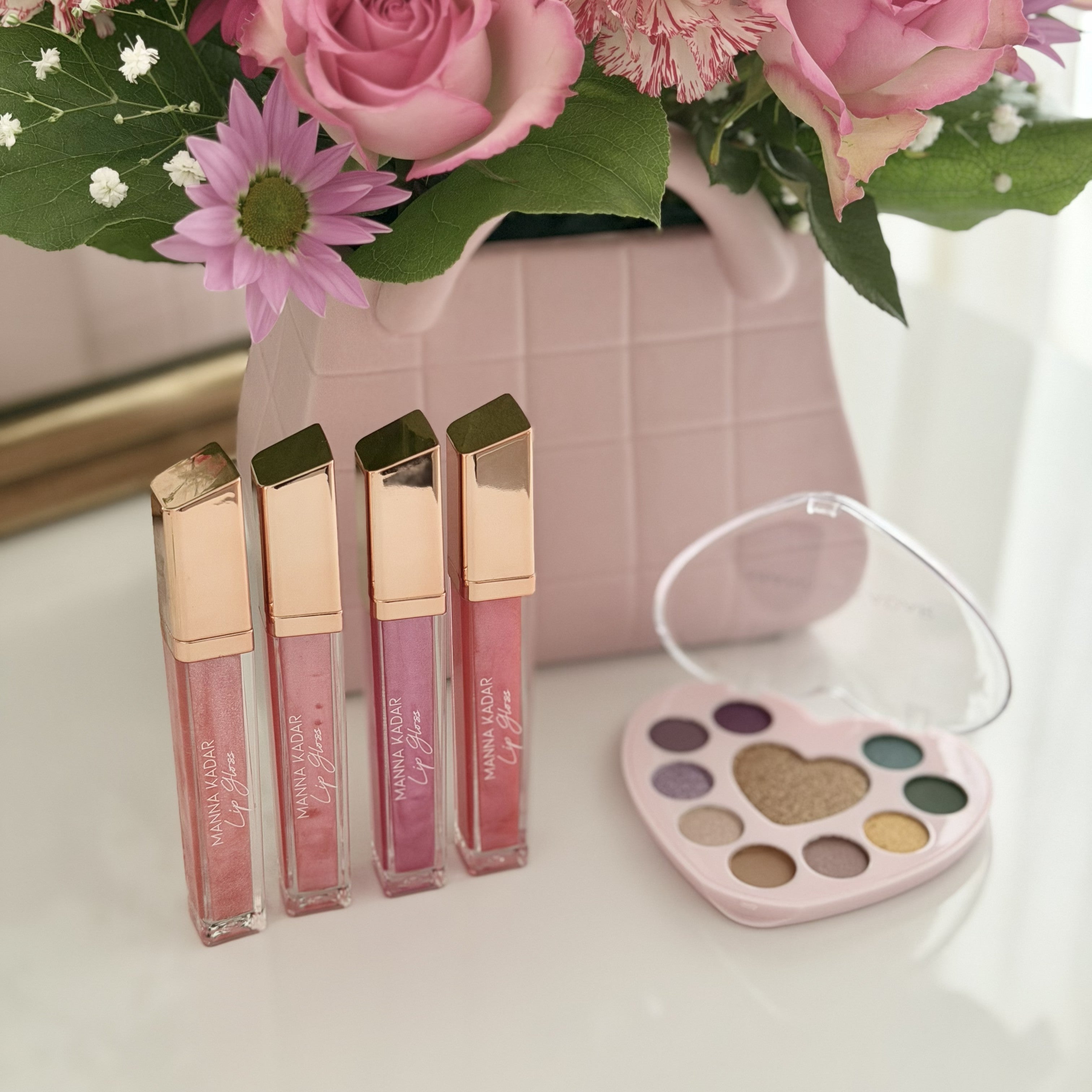Lip glosses and a makeup palette with flowers in the background
