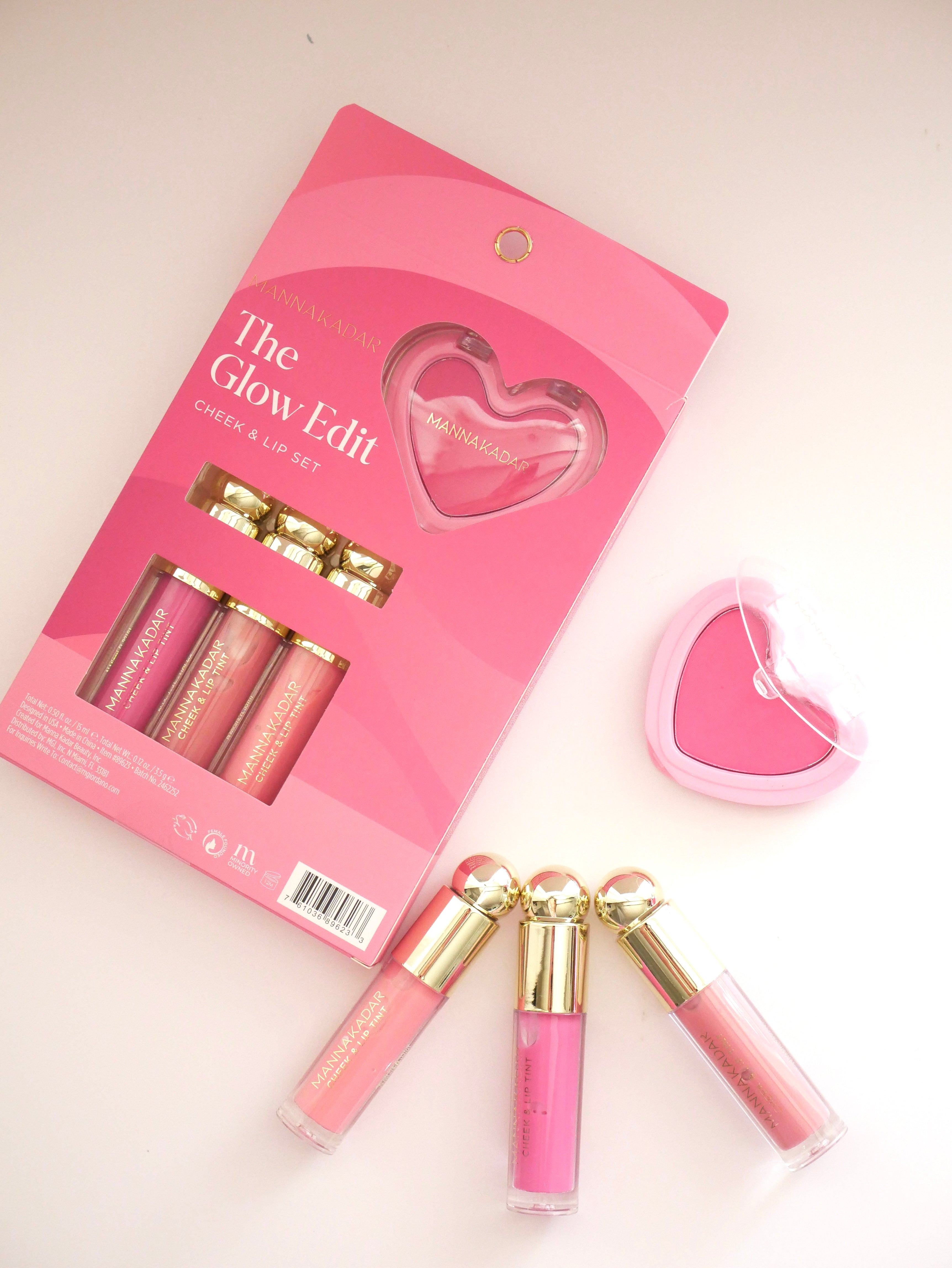 A pink makeup gift set on a white background, featuring a pink package labeled 'The Glow-Edit Cheek & Lip Set' with three lip products and a heart-shaped pink compact.