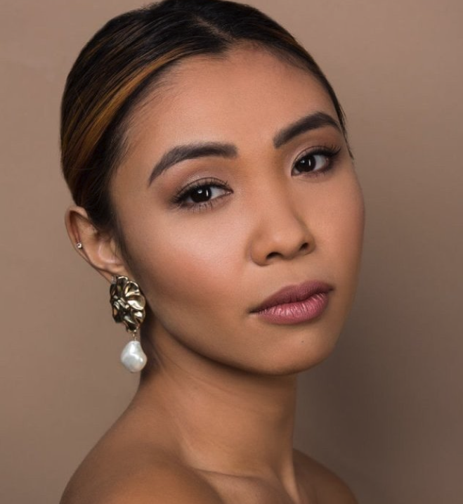 Mid 20's aged woman with slicked back dark hair and clean soft looking makeup showcasing medium tan skin color. Manna Kadar foundation is used for a soft flawless complexion. Gold earing with dangling pearl on soft tan background. 